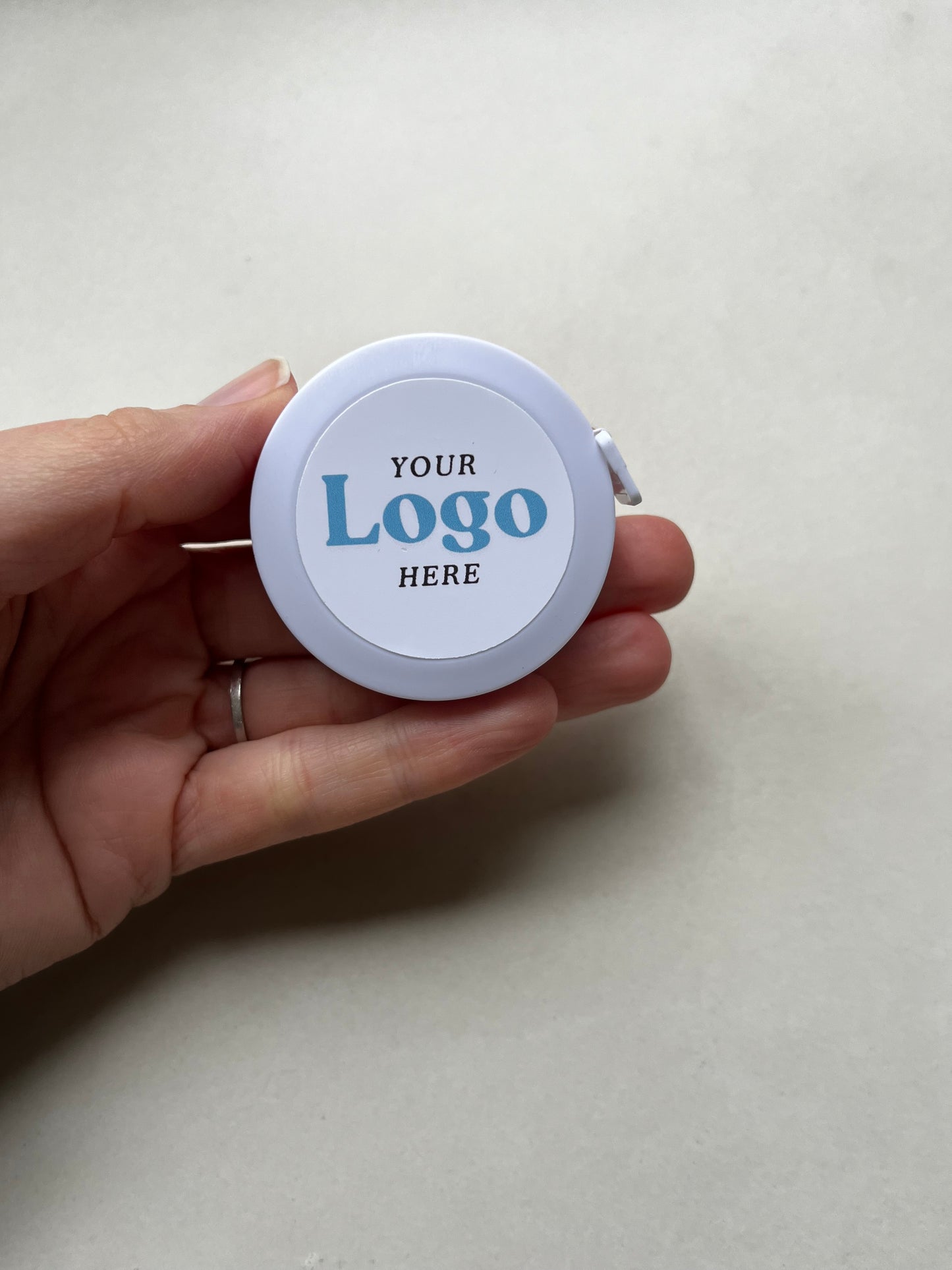 Hand holding a circular tape measure with 'Your Logo Here' text on a plain background