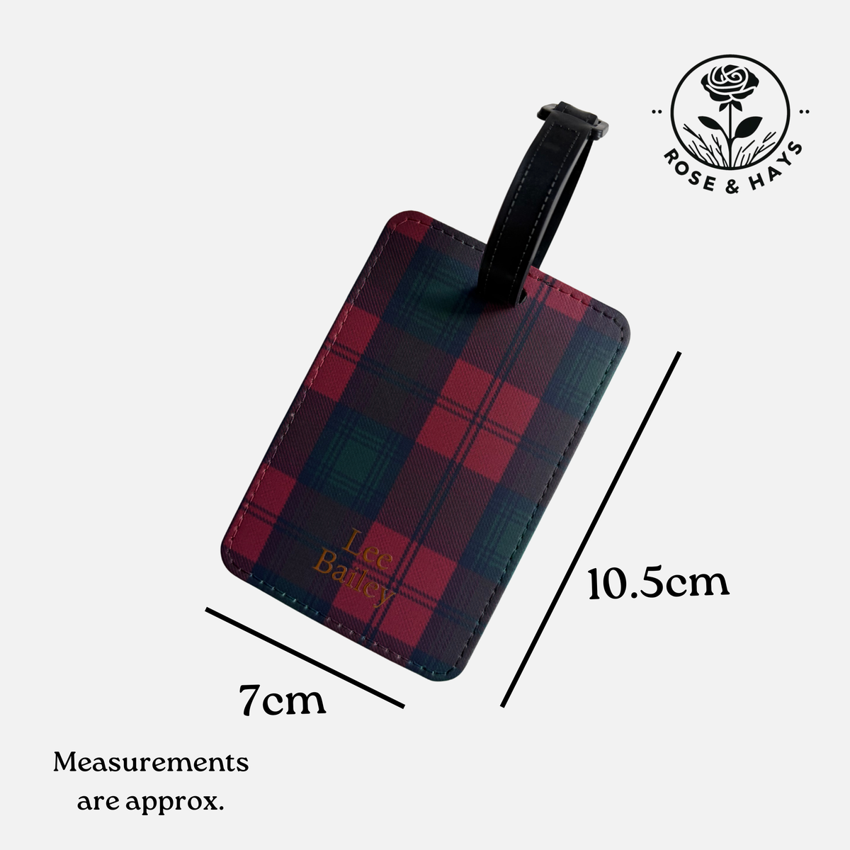 A rectangular luggage tag with a red and dark green tartan plaid pattern, featuring a black strap and gold 'Lee Bailey' personalisation. The image includes dimension lines indicating measurements of 10.5 x 7cm