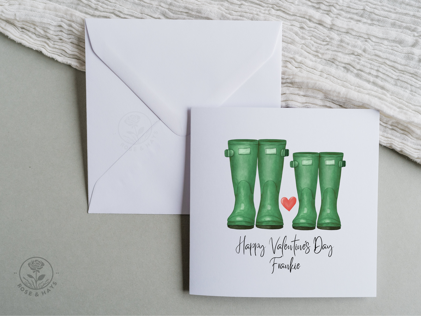 Valentine's Day card with green wellington boots and a heart, featuring an envelope on a gray surface. The card has the text "Happy Valentine's Day Frankie"
