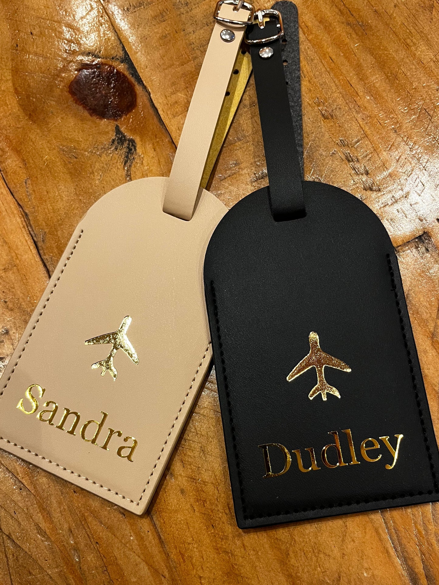 Black and beige luggage tags with engraved names on a wooden surface
