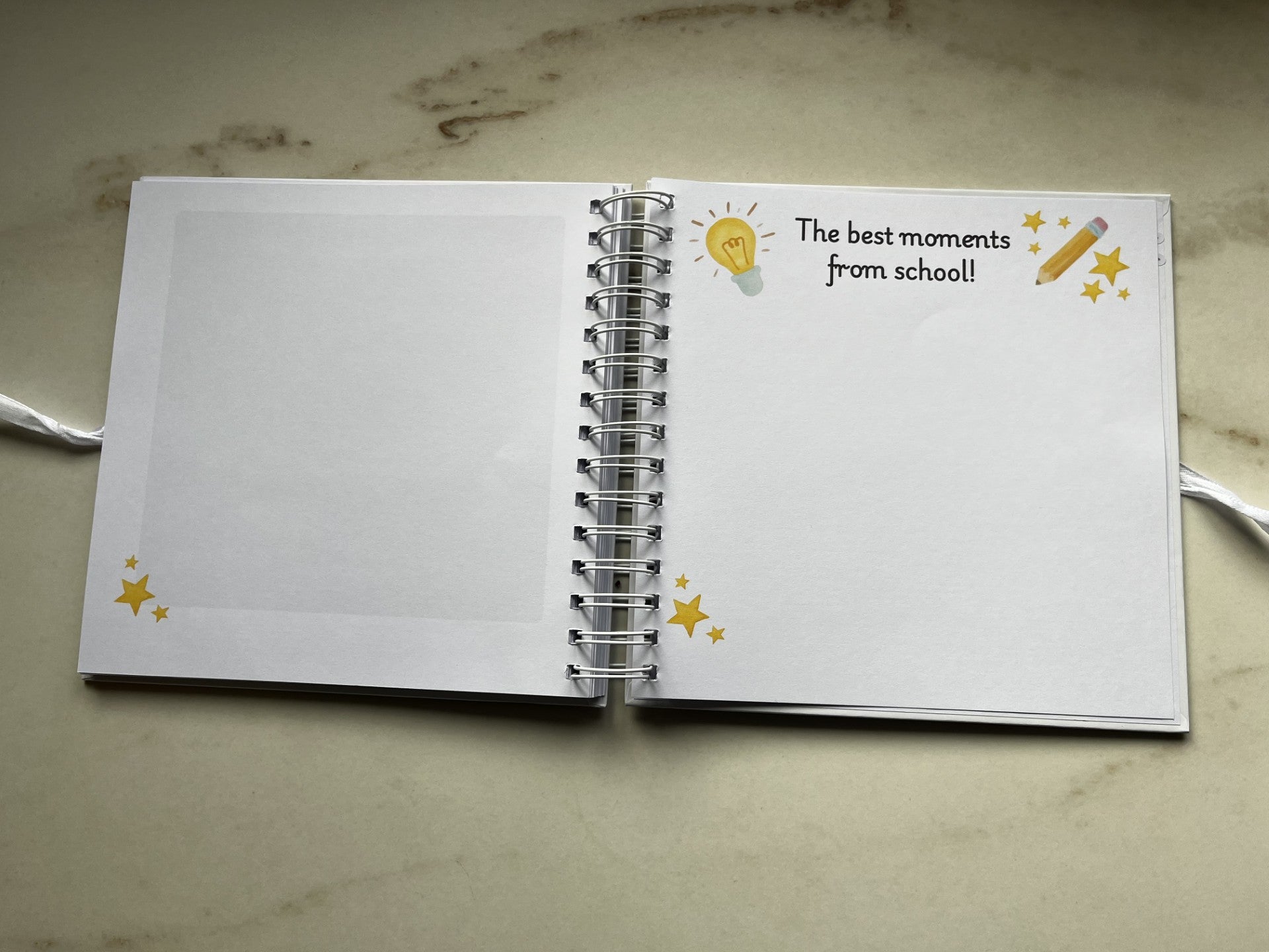Open notebook with decorative cover on a marble surface. The best moments of school. Note memories from primary school