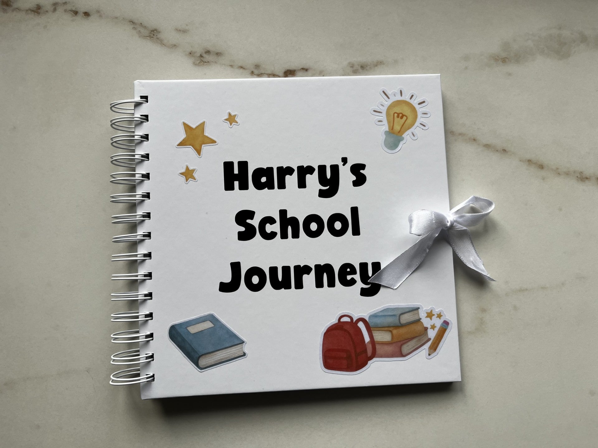 Notebook titled 'Harry's School Journey' with illustrations on a marble surface. School memory book.