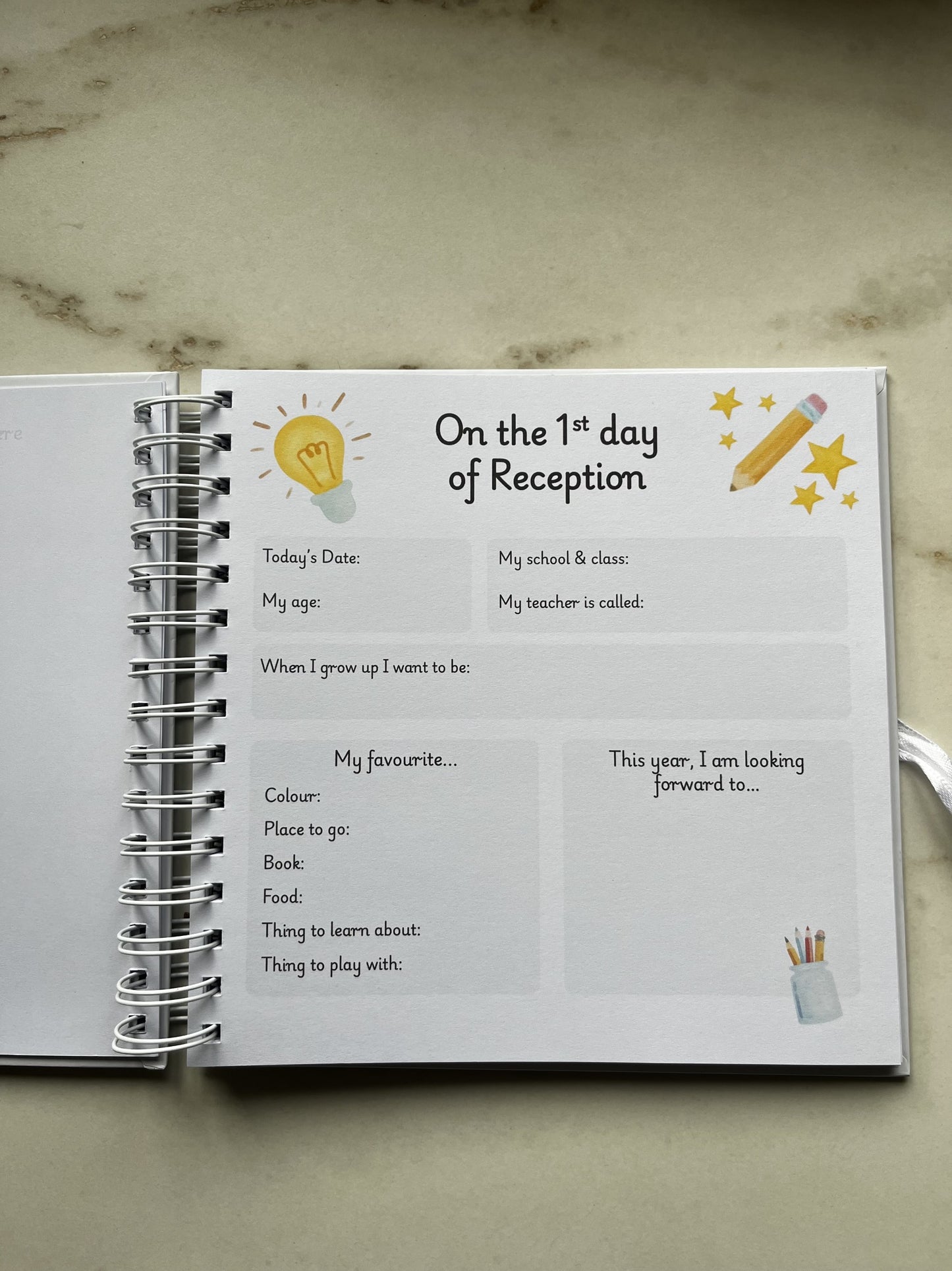 Children's memory scrap book open to a page titled 'On the 1st day of Reception' with illustrations and text. Prompts of information to add to capture memories of the first day of school and reception
